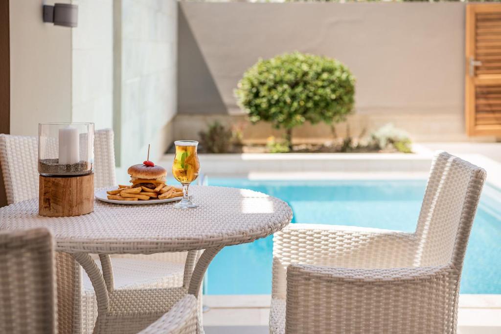 Skaista terase ar baltu rotangpalmu mēbeļu komplektu, uz galda atrodas burgeris ar čili un kartupeļu frī, kā arī gaismas elements, un blakus ir dzēriens. Fons ar baseinu un zaļu krūmu rada relaksējošu atmosfēru.