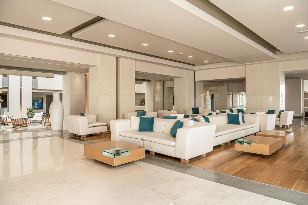 Mūsdienīgs viesnīcas vestibils ar elegantām baltām mēbelēm un zilu aksesuāru, kurā ir plašs atpūtas zonas un dabīgā gaisma.