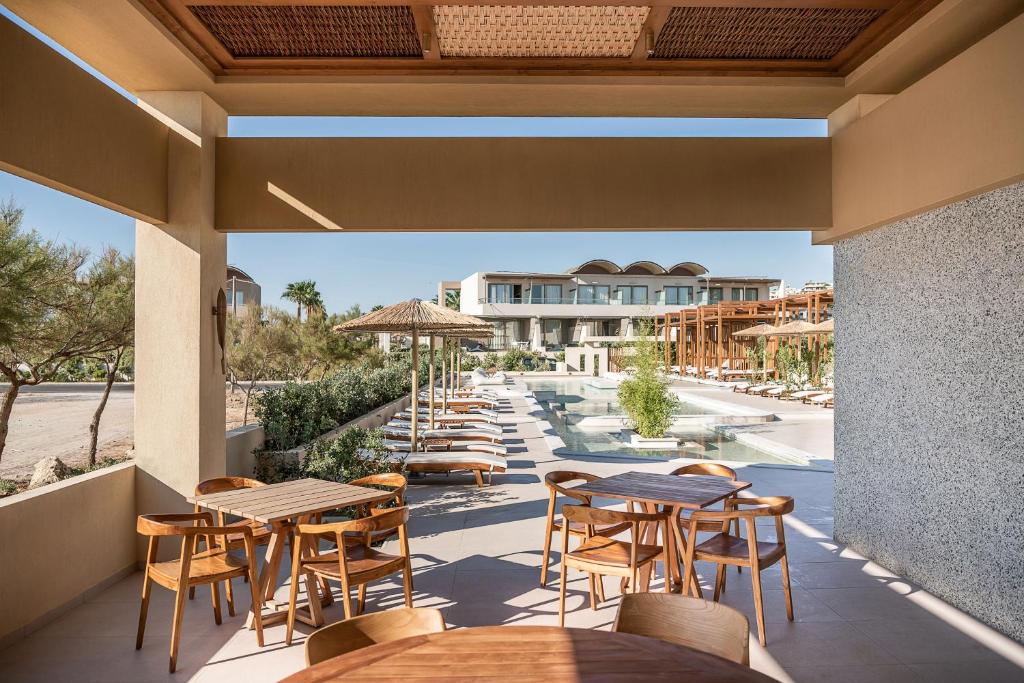 Terase ar koka galdiem un krēsliem, skats uz baseinu un viesnīcu, apkārt augoša zaļums un saule.