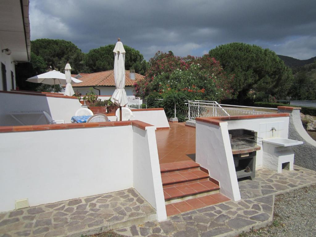 Terase ar balto sienu, flīžu grīdu un grilu, apkārt augošas zaļas augi un sauļošanās krēsli, ideāla vieta atpūtai.