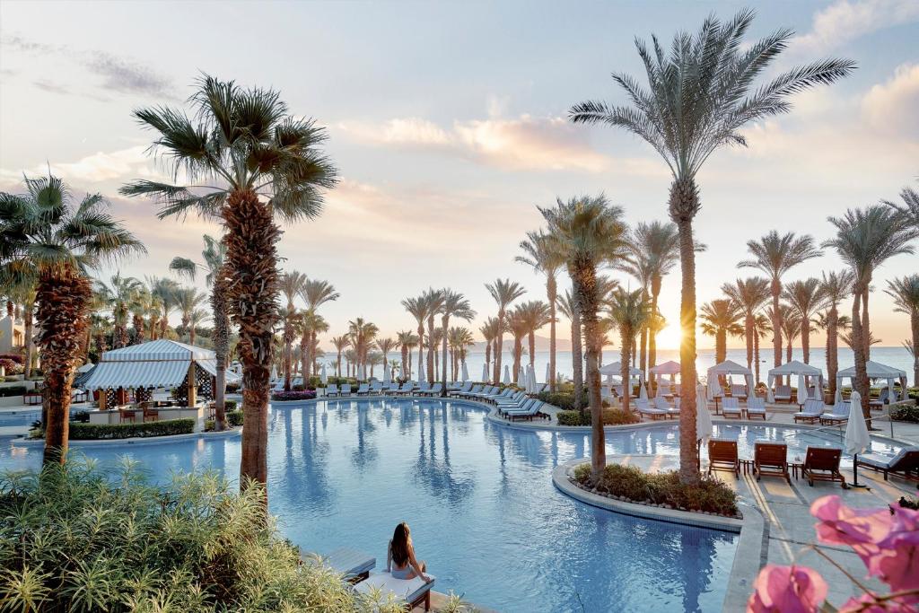 Four Seasons Resort Sharm El Sheikh plašais āra baseins palmu ielokā ar skatu uz jūru saulrietā.