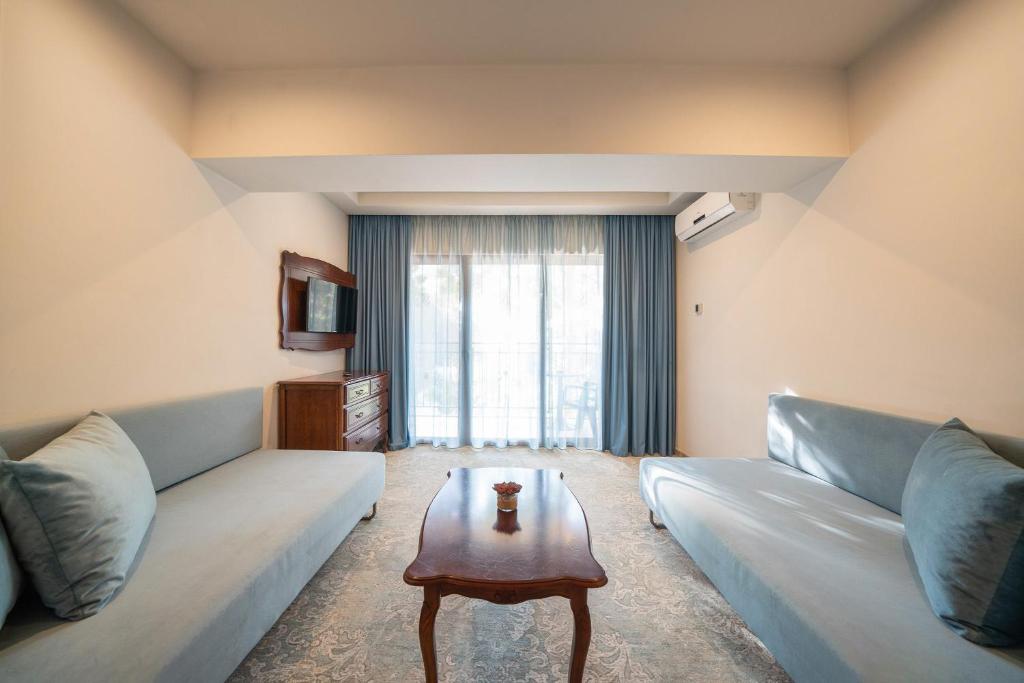 Mūsdienīgs viesnīcas numurs ar divām dīvāngultām, koka galdu un televizoru, kas atrodas blakus balkona durvīm. Gaismas tonis un dekoratīvās detaļas rada mājīgu atmosfēru.