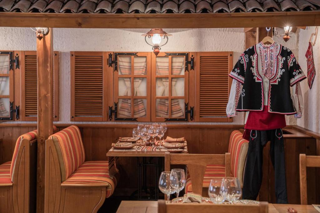 Restorāna interjers ar koka mēbelēm, krāsainām sēdvietām un tradicionālo apģērbu, kas izkārtots pie sienas. Šī vieta rada siltu un viesmīlīgu atmosfēru.