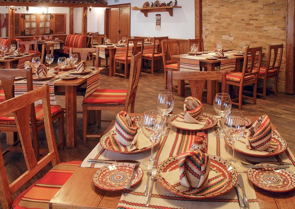 Restorāna interjers ar koka mēbelēm un krāsainiem galda piederumiem, kas izkārtoti uz galdiem ar rakstainām galdautām. Elegants un viesmīlīgs atmosfēras sajūta.