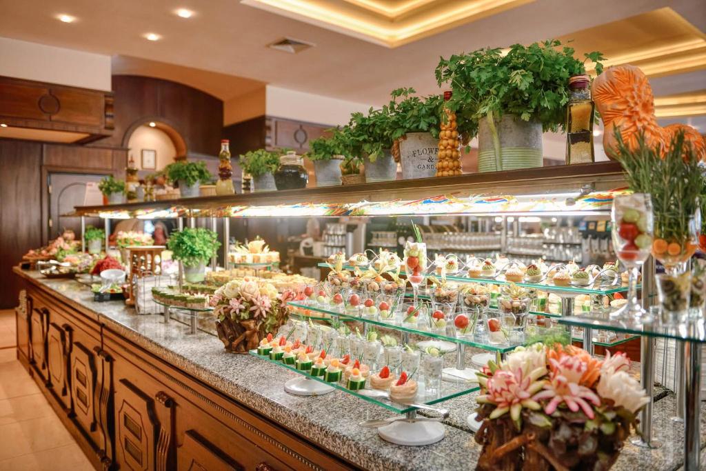 Eleganta bufete ar dažādiem ēdieniem un dekoratīviem ziediem, izvietota uz grezna galda. Bagātīga piedāvājuma izvēle ar krāsainām uzkodām un saldumiem.