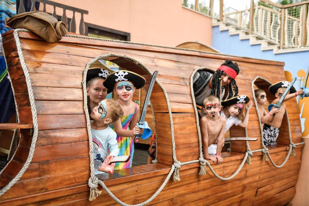 Bērni tērpušies par pirātiem izklaidējas uz koka pirātu kuģa, pozējot ar zobeniem un maskām. Kuģis ir izrotāts ar virvēm un izskatās kā bērnu spēļu laukums.