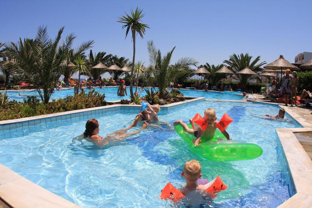 Bērni spēlējas baseinā Mediterraneo Hotel, apkārt palmām un saulei.