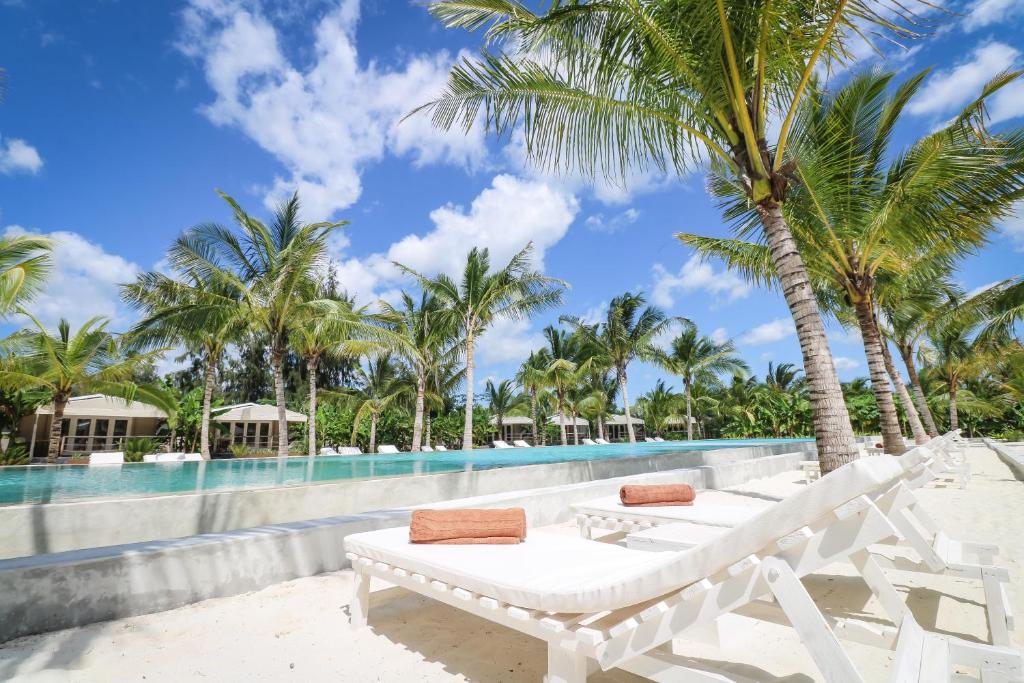 Mwezi Boutique Resort pludmales atpūtas zona ar palmām un baseinu.