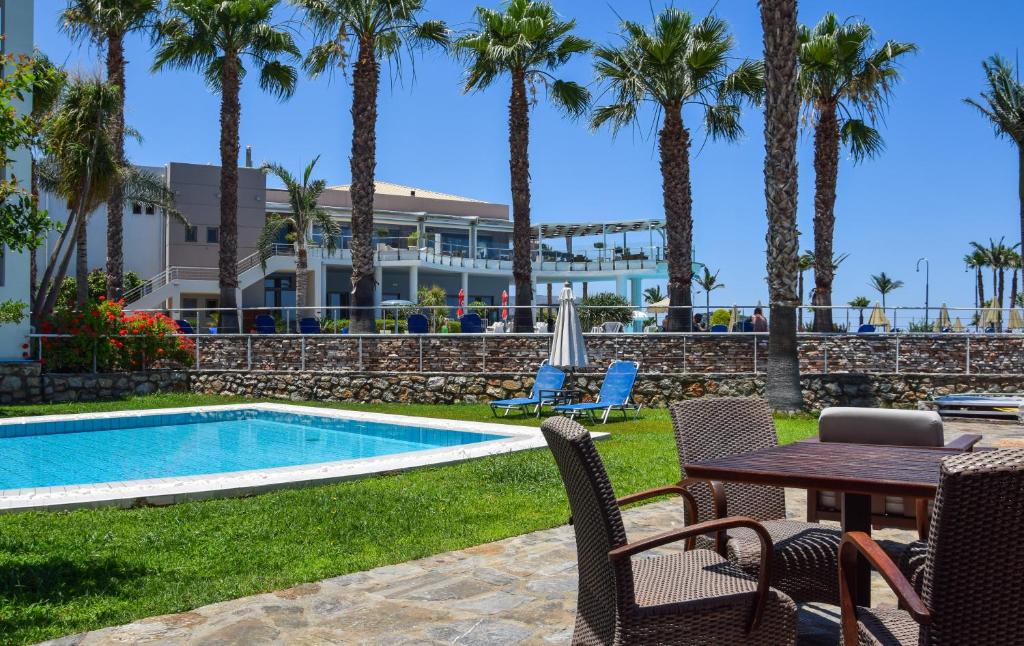 Vasaras atpūtas vieta ar baseinu, palmu kokiem un mājīgu atpūtas zonu. Skats uz viesnīcu un skaistu ainavu ar zāles laukumu un saulessargiem.