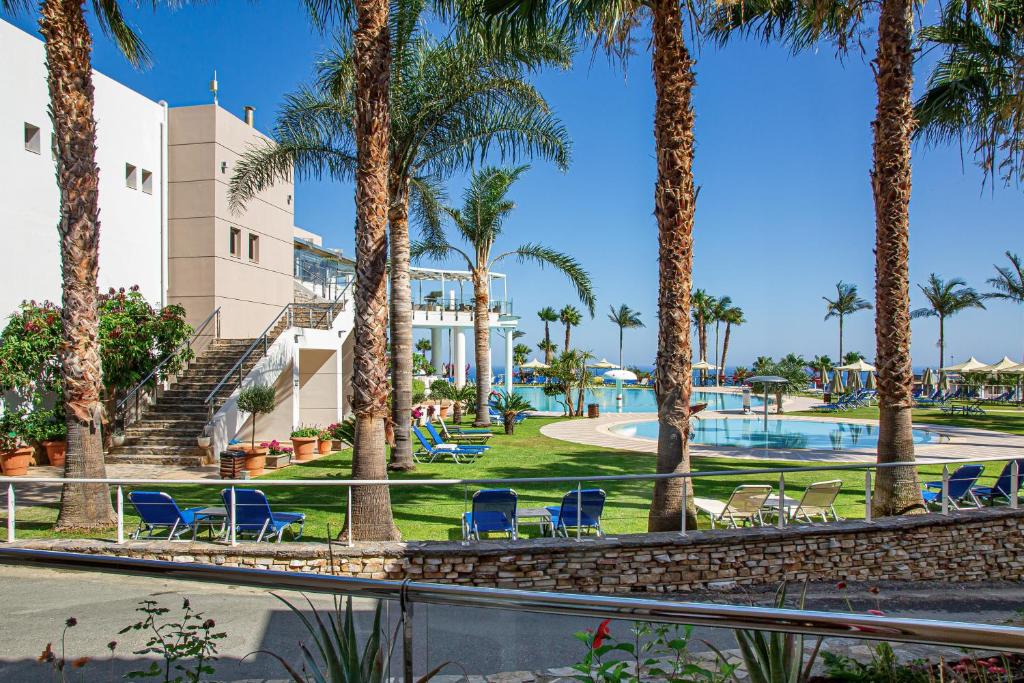 Vasaras atpūtas vieta ar palmām, baseinu un sauļošanās krēsliem, kas piedāvā relaksējošu atmosfēru. Apkārt ir zaļā zāle un skaidrs debesis.