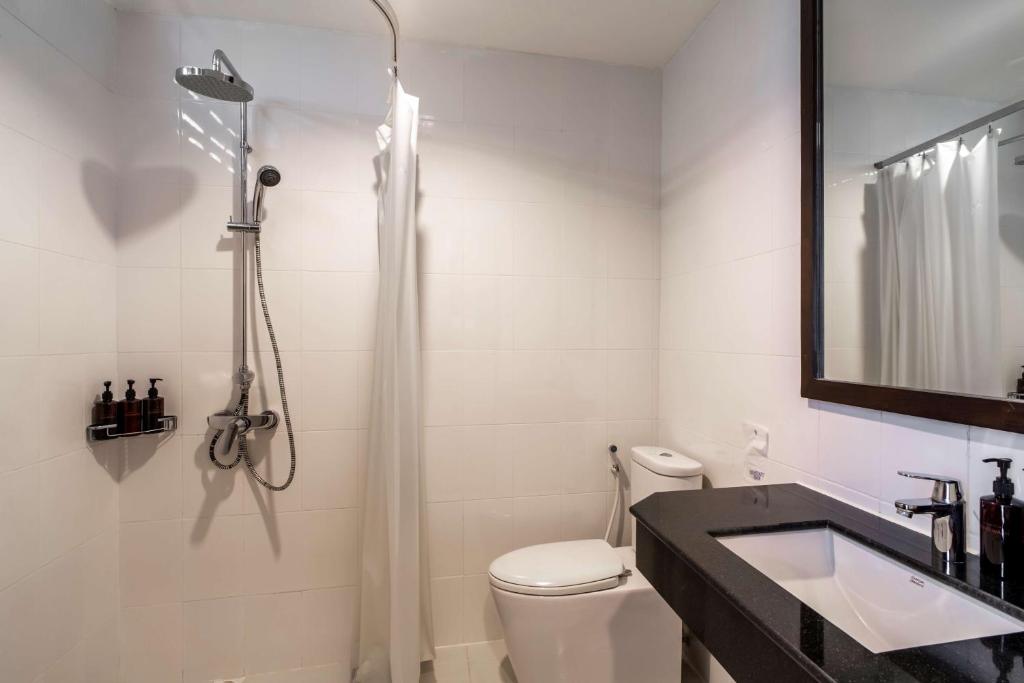 Mūsdienīgs vannas istabas interjers ar dušu, tualeti un melnu izlietni, papildināts ar higiēnas līdzekļiem un spoguli.