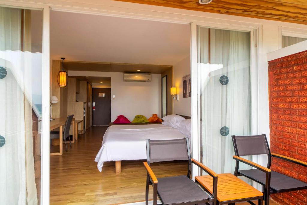 Mūsdienīgs viesnīcas numurs ar balkonu, kurā ir divguļamā gulta, rakstāmgalds un krēsli, kā arī spilgti krāsainas spilvenu apdare.