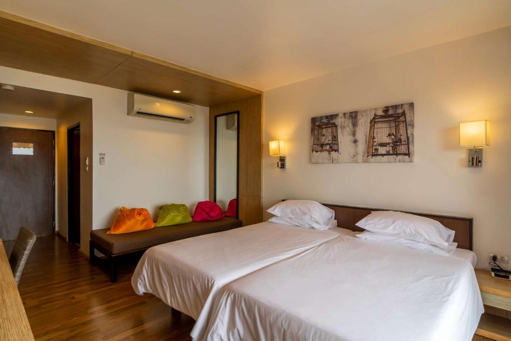 Mūsdienīga viesnīcas numura interjers ar divām gultām, koka grīdu un krāsainiem spilveniem sēdvietā. Sienas rotā mākslas darbs ar putnu būrīšiem.