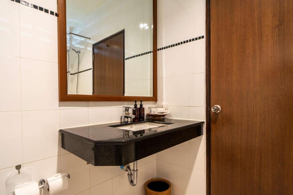 Mūsdienīgs vannasistabas dizains ar melnu akmens izlietni, spoguli un koka durvīm, kas rada elegantu atmosfēru. Vannasistabā ir arī higiēnas piederumi un papīra dvieļi.