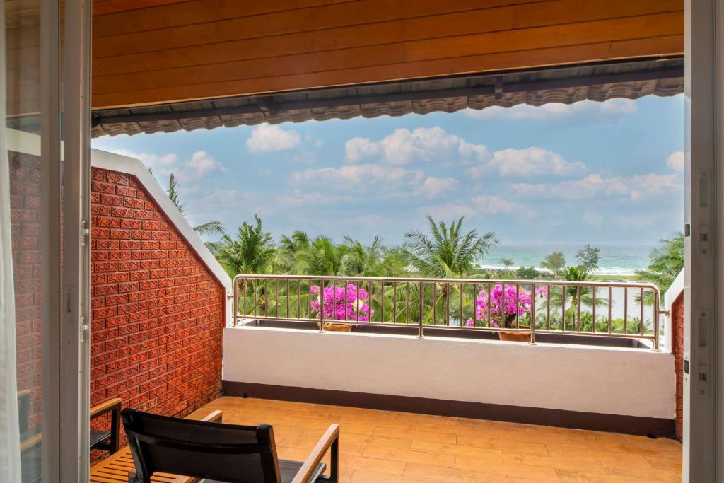 Skats no balkona uz jūru, kur redzami palmas un ziedošas orhidejas. Gaisīgs atmosfēras noskaņojums ar mākoņainu debesu fonu.