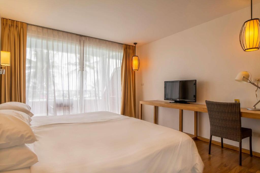 Moderns viesnīcas numurs ar divām gultām, koka grīdu un lieliem logiem, caur kuriem ieplūst dabiska gaisma. Numurā ir televizors un darba galds ar krēslu.