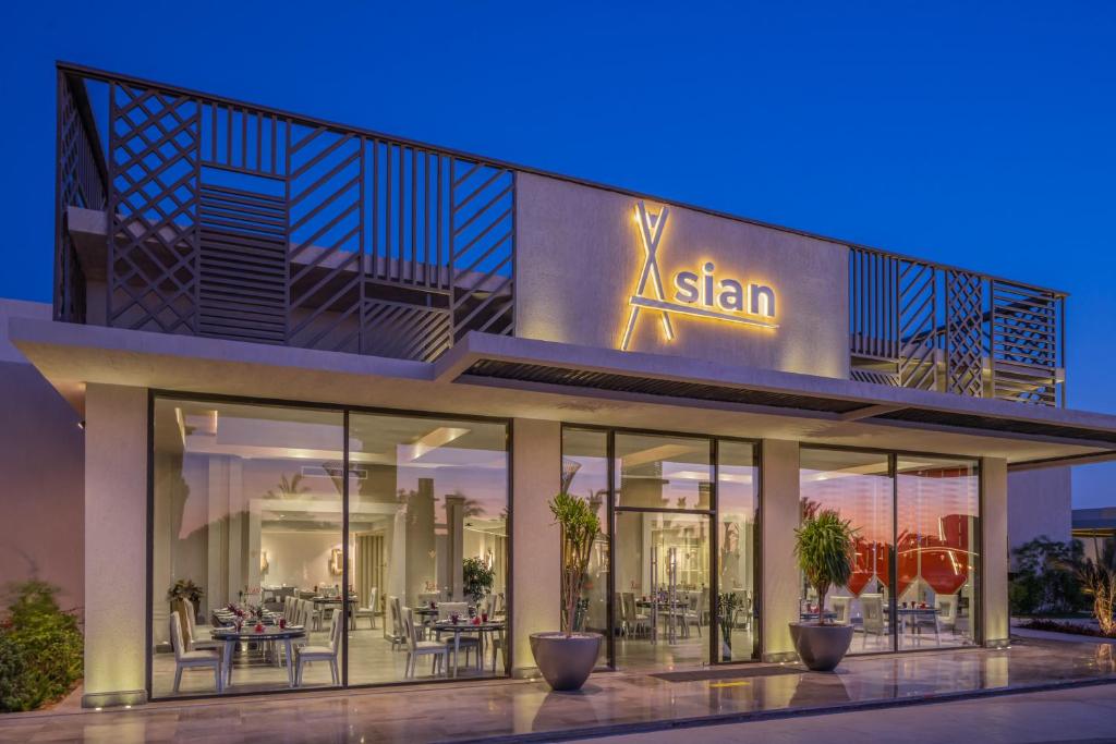 Moderns restorāna ēkas eksterjers ar izgaismoto nosaukumu "Xsian" un plašām stikla sienām, kas atklāj elegantu iekštelpu dizainu. Apzaļumojums papildina atmosfēru.