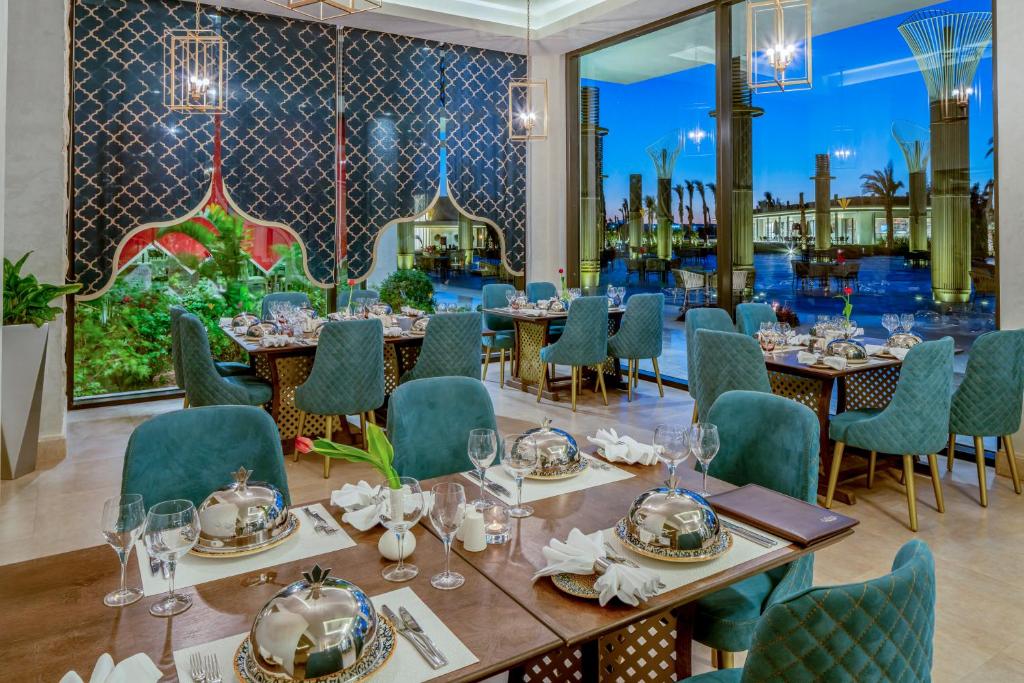 Elegantā restorāna interjers ar zilu apgaismojumu un greznu galdu klājumu, kas piedāvā skatu uz ārējo dārzu un baseinu. Moderns un stilīgs dizains rada patīkamu atmosfēru.
