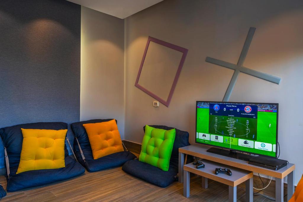 Mūsdienīga spēļu istaba ar ērtiem sēdekļiem un televizoru, kurā tiek rādīts futbola spēles ekrāns. Krāsaini spilveni un stilīgs interjers piešķir telpai dzīvīgumu.