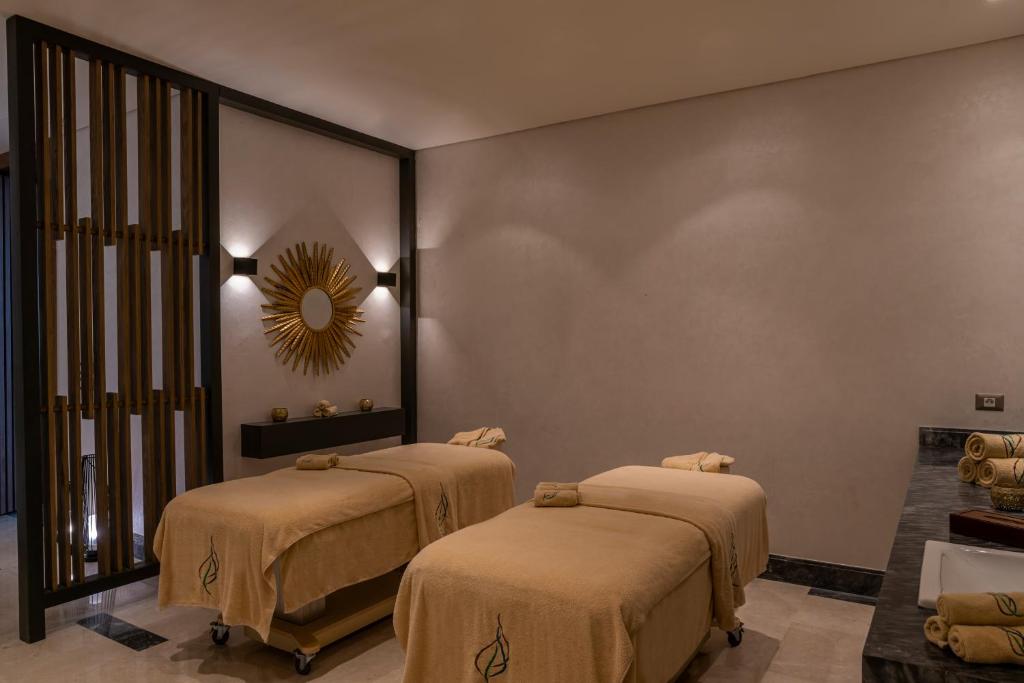 Mūsdienīgs spa interjers ar divām masāžas galdiem, apklāti ar zeltainām dvielēm, un elegantu spoguli uz sienas. Telpu papildina maiga apgaismojums un stilīgs dekorējums, radot relaksējošu atmosfēru.