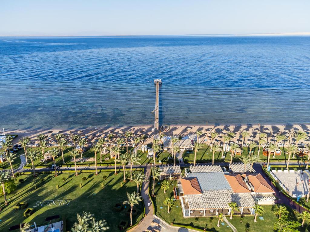 Rixos Sharm El Sheikh viesnīcas piekrastes skats ar palmām un pludmales gultām.