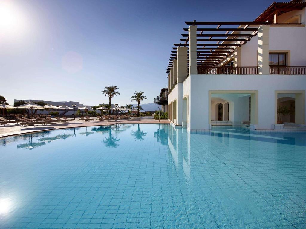 Creta Maris Resort baseins ar palmām un sauli, relaksējoša atmosfēra.