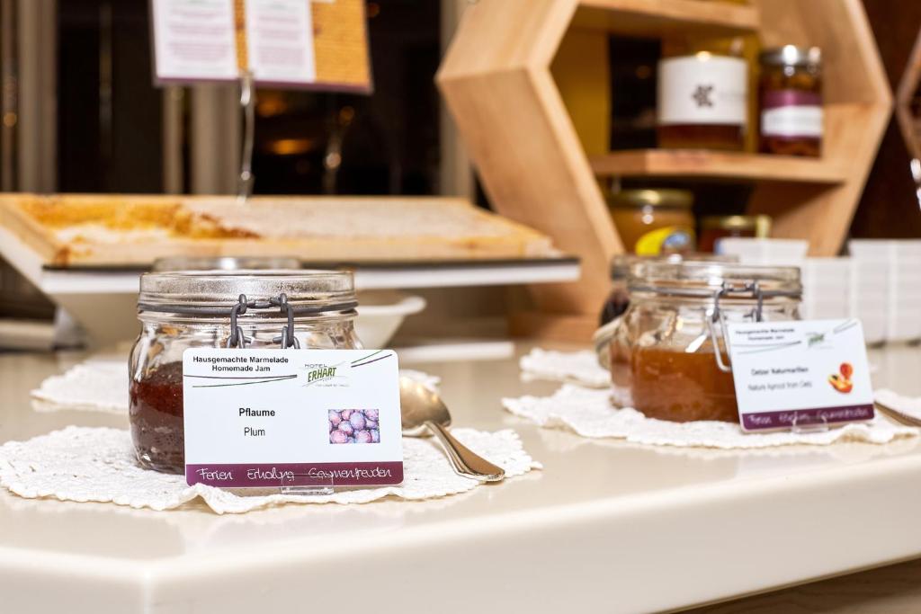 Mājās gatavota marmelāde ar plūmju un persiku garšām, pasniegta stikla burciņās uz galda. Marmelādes ir noformētas ar nosaukumiem un attēliem, kas norāda to sastāvu.