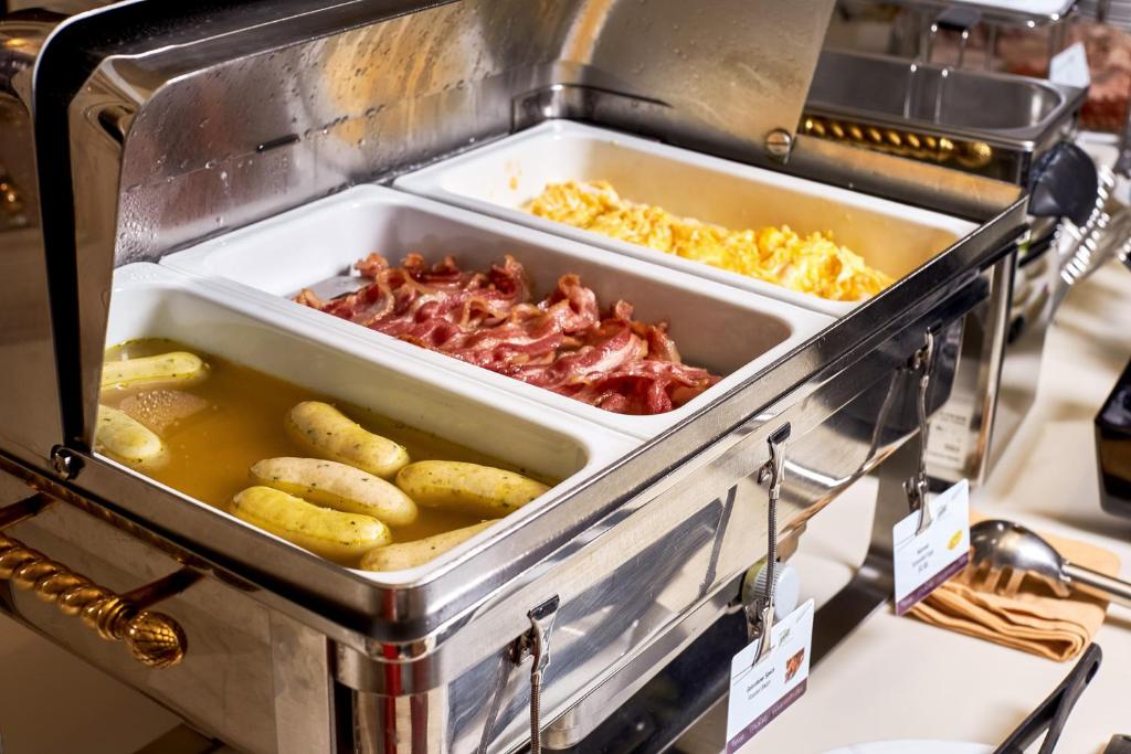 Siltā ēdienu pasniegšanas stacija ar ceptu speķi, vārītiem desiņām un omleti, kas gaida viesus brokastīs.