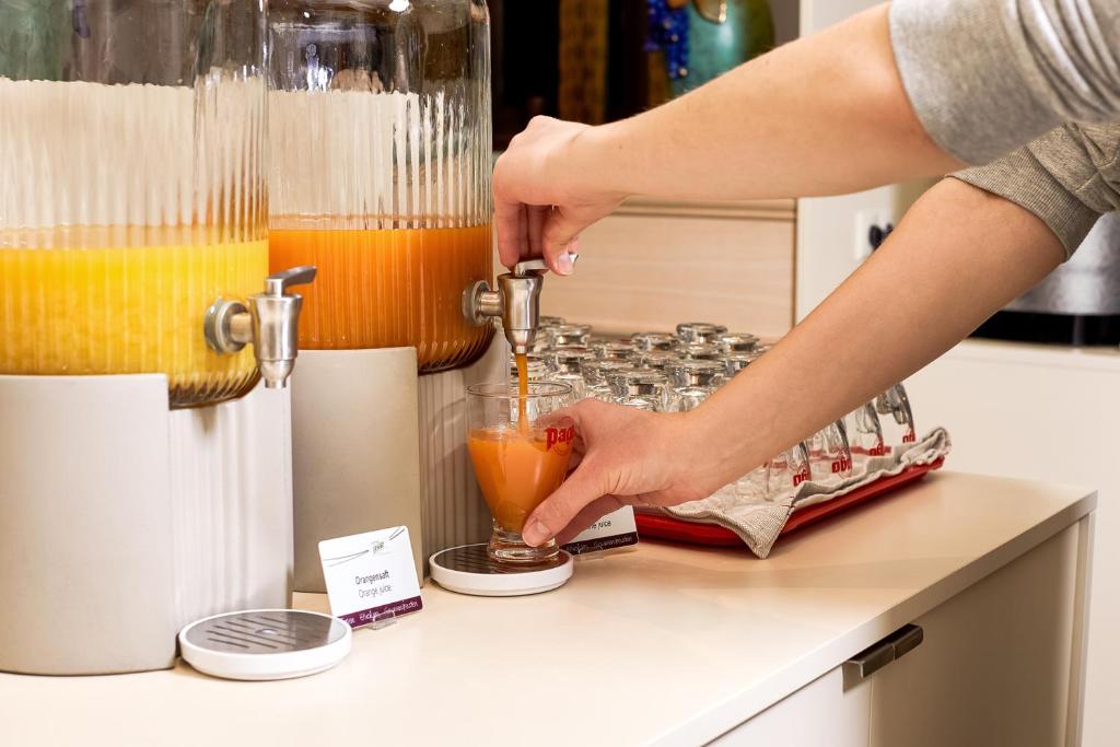 Svaigā apelsīnu un ingvera sulas izsniegšana no dzērienu dozatoriem, ar roku, kas tur glāzi, lai piepildītu to.