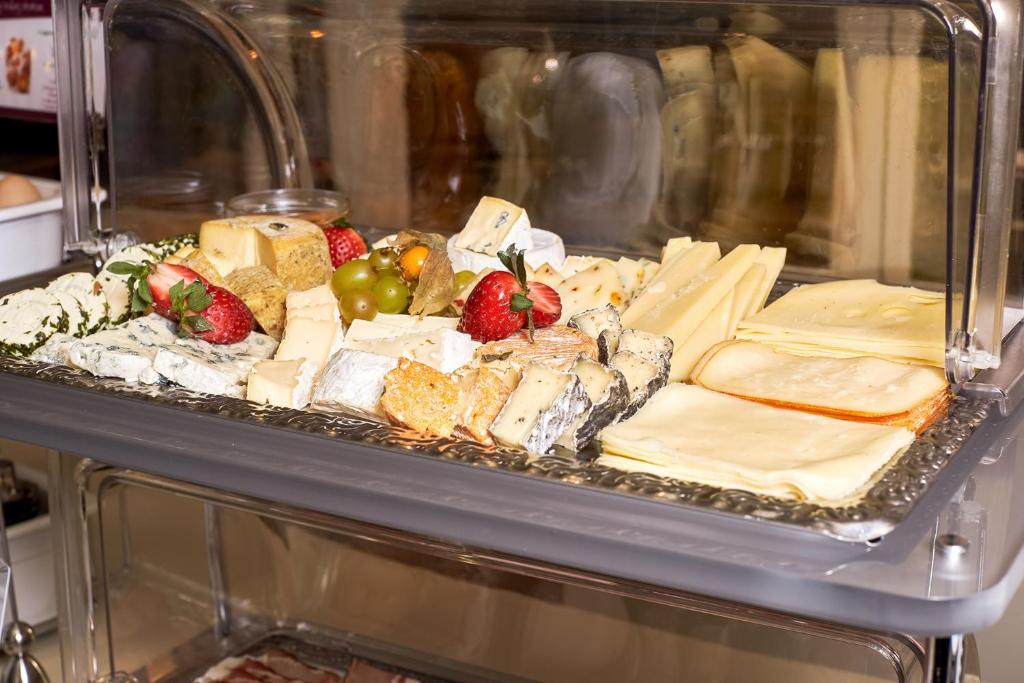 Siera plāksne ar dažādiem sieriem, ogām un vīnogām, pasniegta stikla vitrīnā.