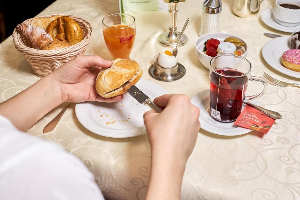 Brokastu galds ar maizītēm, augļu salātiem un tēju, kurā cilvēks sagriež maizi. Izsmalcināta brokastu atmosfēra.