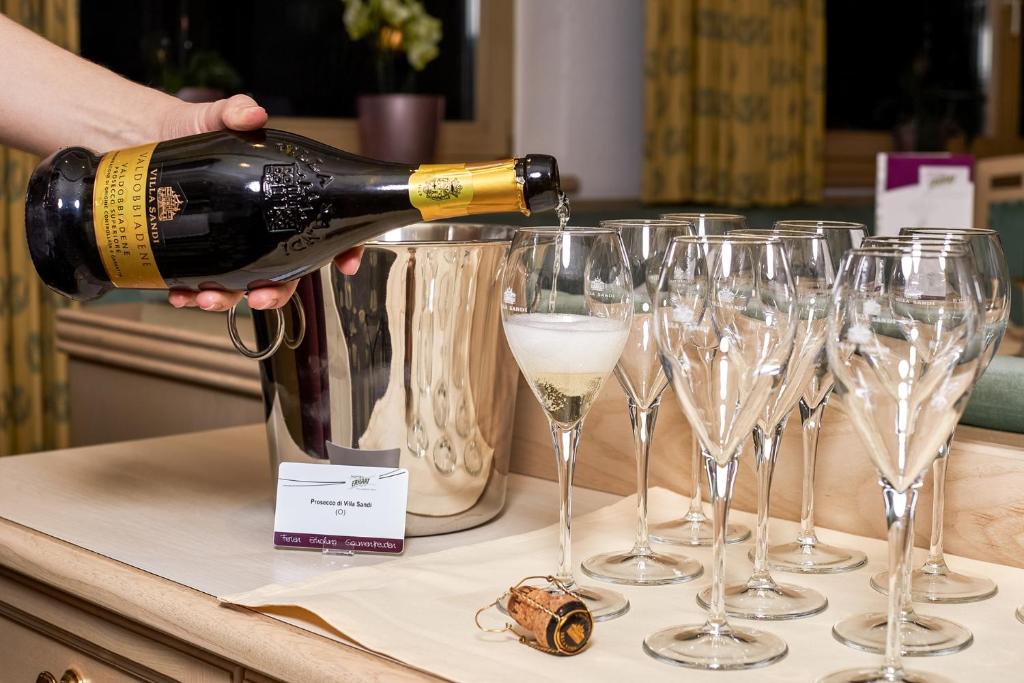 Šampanieša pudele tiek izlieta glāzē, blakus ir vairākas tukšas glāzes un ledus spainis. Uz galda ir arī kartīte ar dzēriena nosaukumu.