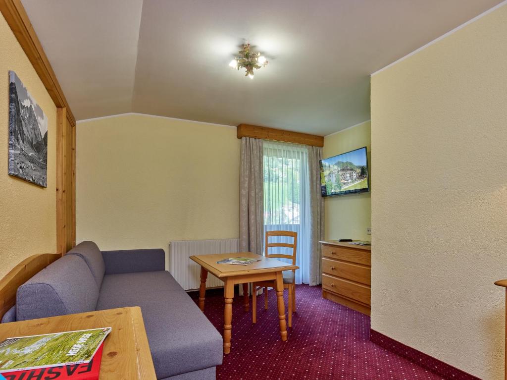 Mūsdienīga viesnīcas istaba ar dīvānu, koka galdu un televizoru, kas atrodas pie loga ar skatu uz dabu. Siltas krāsas un mājīga atmosfēra.