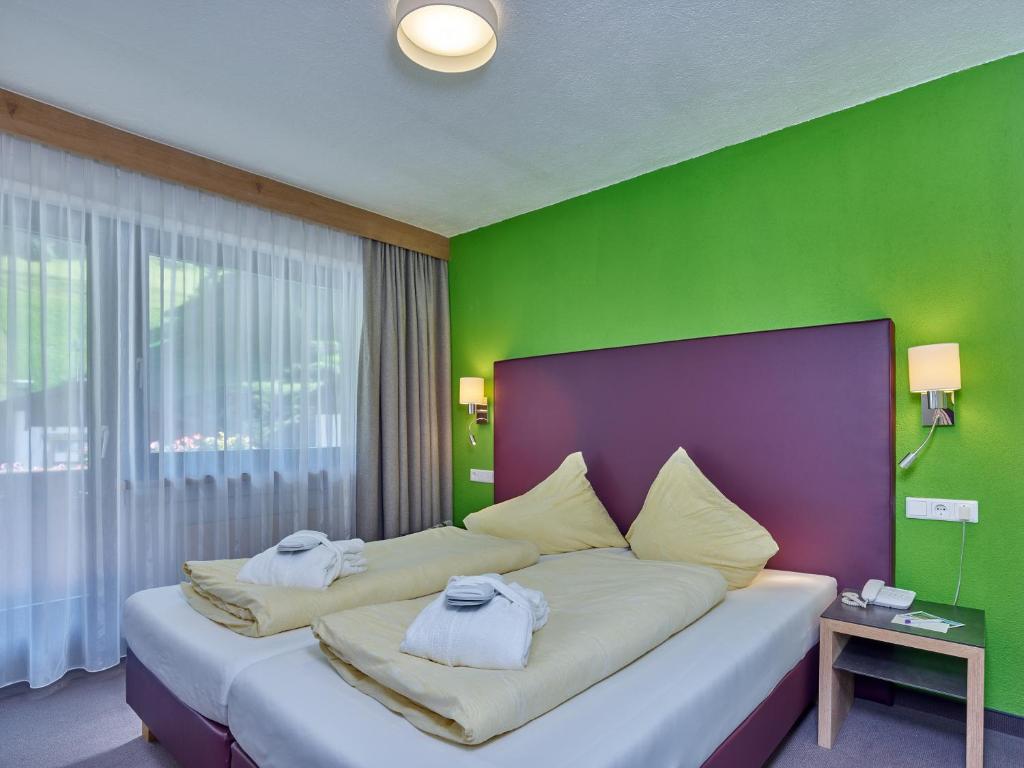 Mūsdienīgs viesnīcas numurs ar spilgti zaļu sienu, divām gultām un dabīgu apgaismojumu, kas rada mājīgu atmosfēru. Ideāli piemērots relaksējošai atpūtai.