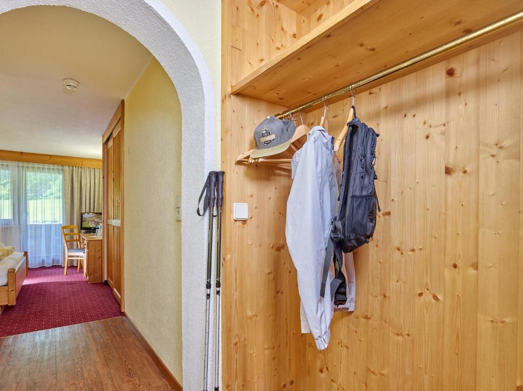 Korpusa ar koka apdari un drēbju pakaramajiem, kur karājas krekls un mugursoma, redzams ieejas ceļš uz viesistabu. Interjers ir gaišs un viesmīlīgs, radot mājīgu atmosfēru.