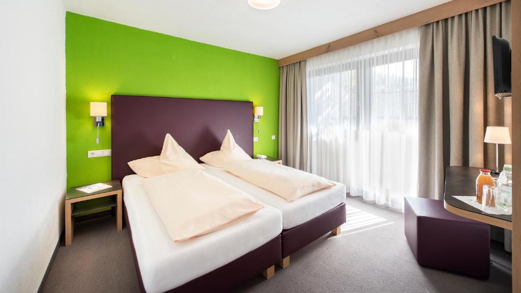 Mūsdienīgs viesnīcas numurs ar divām gultām, ko ieskauj spilgti zaļa siena un dabisks apgaismojums. Numurā ir koka galdiņš un ērtas drēbes, kas rada patīkamu atmosfēru.