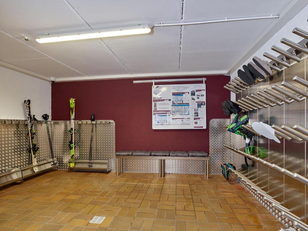 Ski aprīkojuma uzglabāšanas telpa ar slēpju turētājiem un sēdvietām, kas paredzēta sporta entuziastiem. Telpa ir sakārtota un ērta, nodrošinot vietu ekipējuma novietošanai.