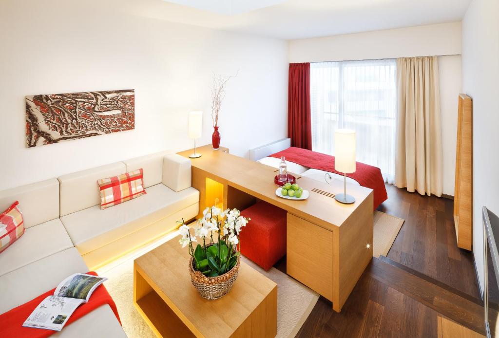 Mūsdienīgs viesnīcas numurs ar gaišu interjeru, ērtu dīvānu un koka galdu, uz kura novietoti augļi un ziedi. Logi ar aizkariem nodrošina dabisko apgaismojumu.