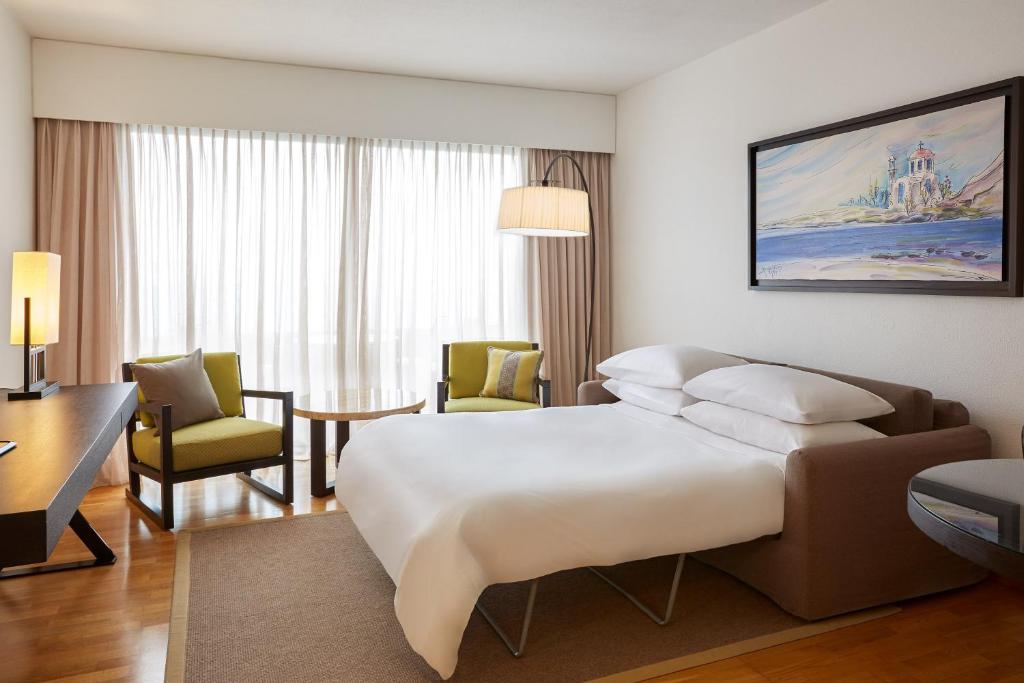 Mūsdienīgs numurs ar gultu, dīvānu un skatu uz dabu, Sheraton Rhodes Resort.