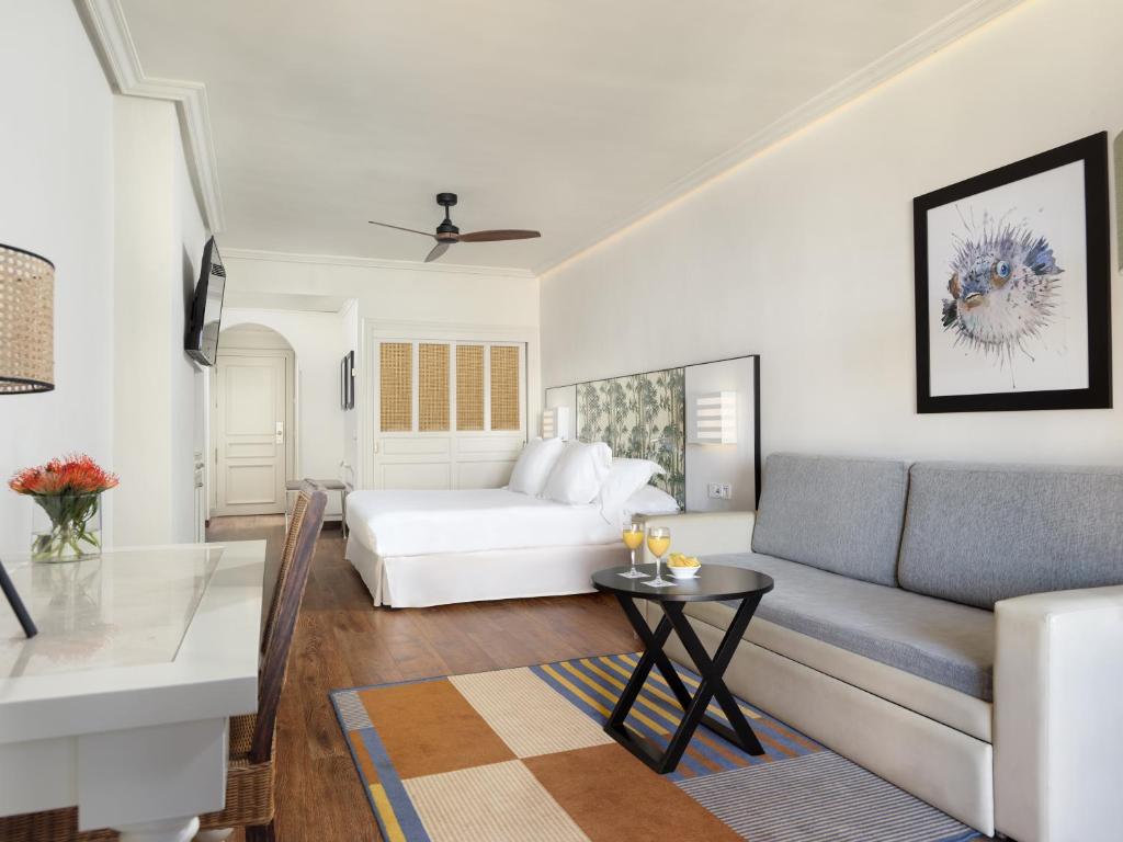 Mūsdienīgs viesnīcas numurs ar gultu, dīvānu un televizoru. Telpā ir elegants galds un dekoratīvas gleznas, radot patīkamu atmosfēru.