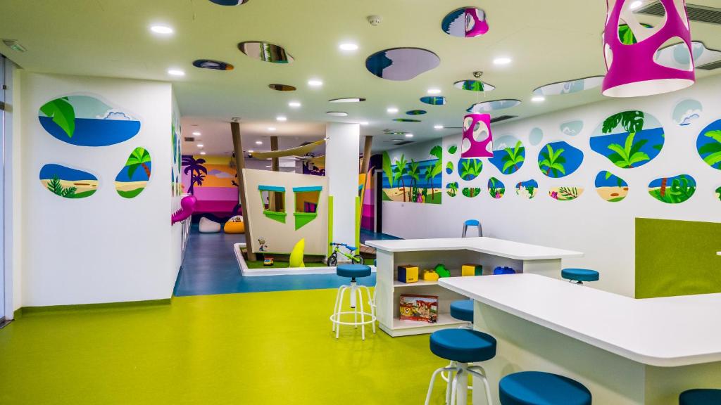 Krāsaina bērnu rotaļu istaba ar interaktīvām sienām un jautrām dekorācijām, kas veicina radošumu un spēles. Telpa ir gaiša un draudzīga, ar dažādām aktivitātēm bērniem.