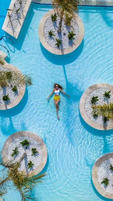 Sieviete peld baseinā starp zaļiem augiem pie Liberty Hotels Lara.