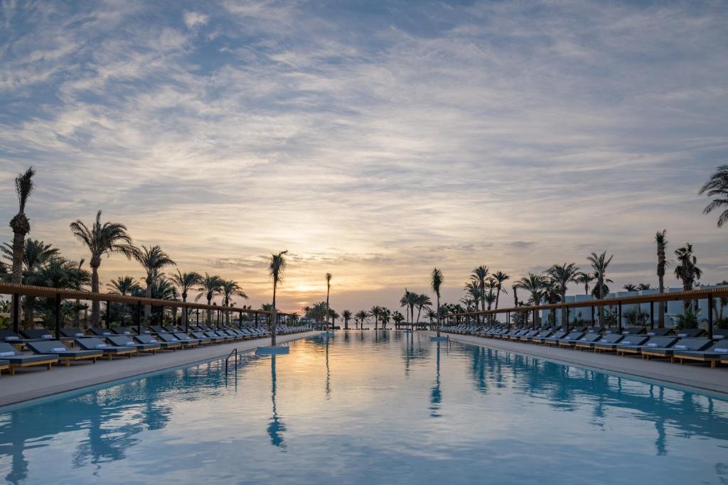 Serry Beach Resort baseins piekrastē ar palmām un saulrietu.