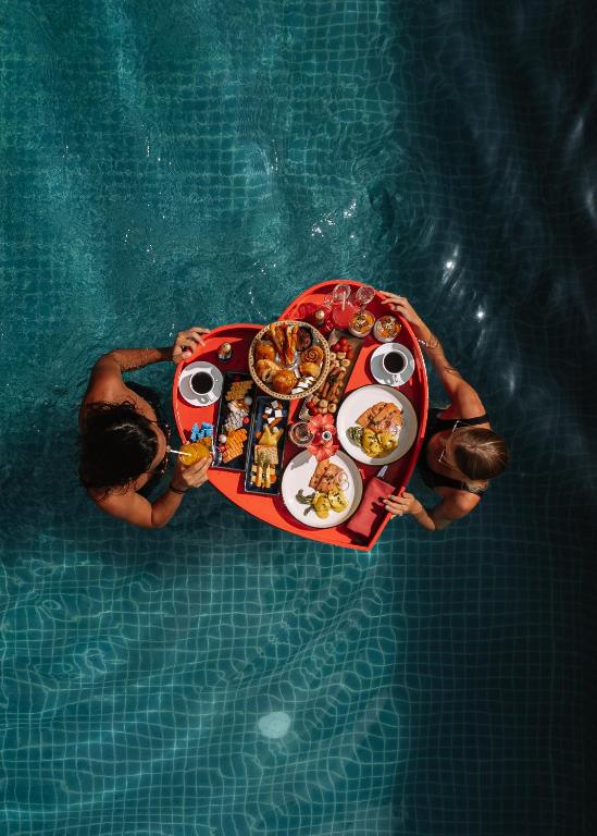 Sirds formas peldbaseina paplāte ar dažādiem ēdieniem un dzērieniem, ko dalās divas sievietes. Ideāla brīvdienu atmosfēra.