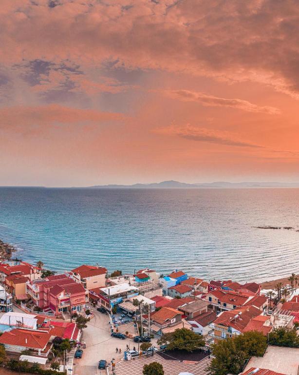 Pilsētas ainava ar krāsainām mājām un jūru, kas izstiepjās līdz horizontam, kamēr debesīs ir siltas krāsas un mākoņi.