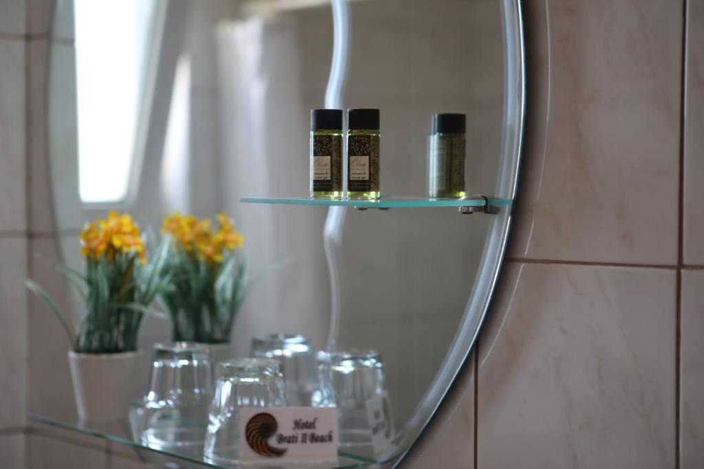 Stikla plauktā ir divas eļļu pudeles un ziedu kompozīcija, kas piešķir telpai mājīgu atmosfēru. Apakšā redzami glāzes un viesnīcas nosaukums.