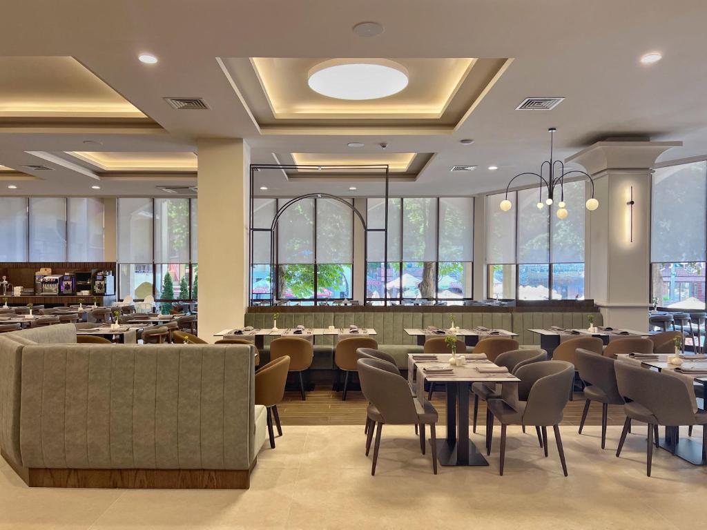 Mūsdienīgs restorāna interjers ar elegantiem galdiem un krēsliem, gaišu apgaismojumu un plašām logu ailēm, kas sniedz skatu uz ārpusi.