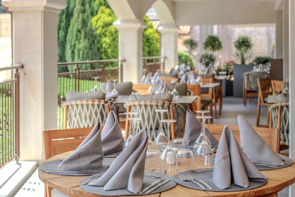 Eleganta restorāna terase ar gaumīgi klātiem galdiem, uz kuriem ir auduma salvetes un glāzes. Zaļie augi un modernais interjers rada patīkamu atmosfēru.