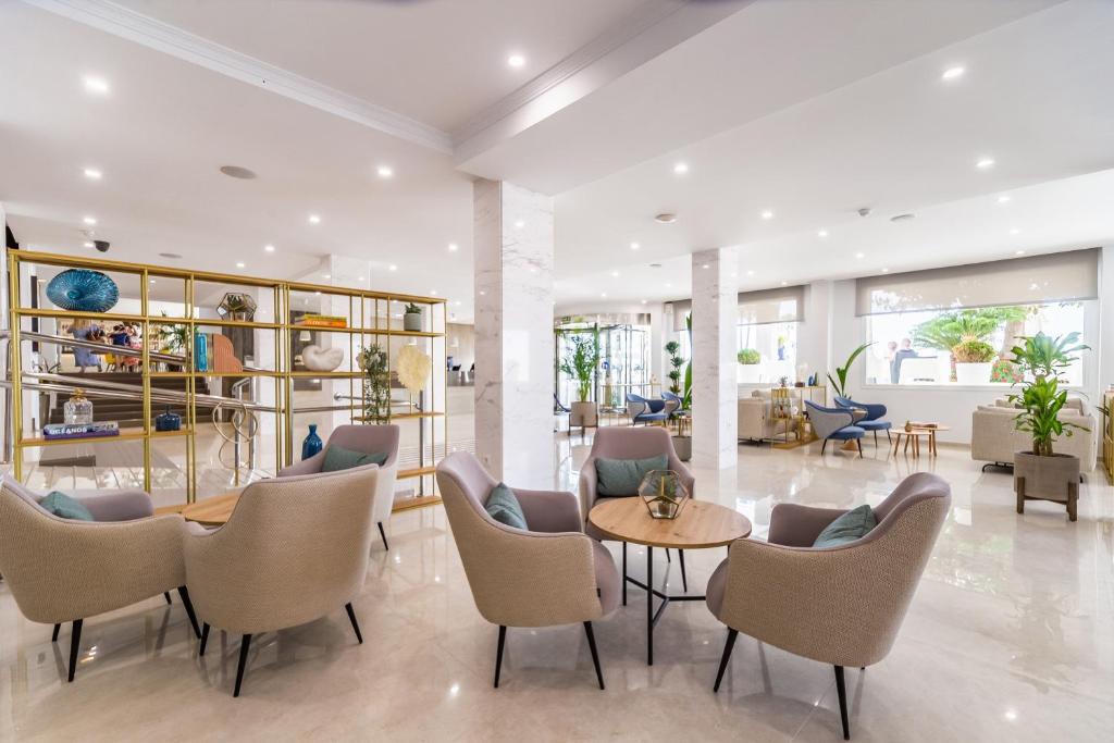 Mūsdienīgs viesnīcas vestibils ar elegantiem krēsliem, modernu dekoru un zaļām augiem, kas rada viesmīlīgu atmosfēru. Gaismas un plašums uzsver telpas šarmu.