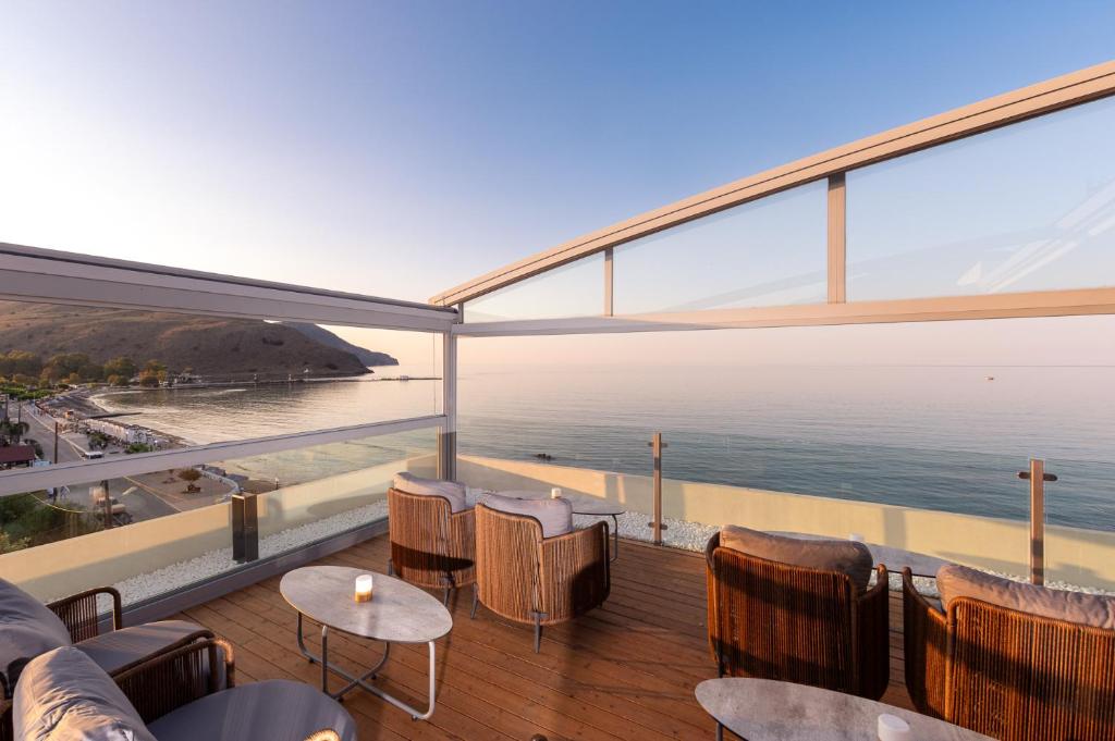 Moderns balkons ar ērtiem krēsliem un galdu, no kura paveras skats uz mierīgu jūru un kalnu ainavu. Saules gaisma izgaismo telpu, radot relaksējošu atmosfēru.